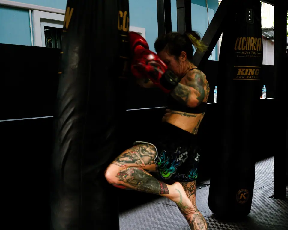 A woman throwing a knee into a heavy bag